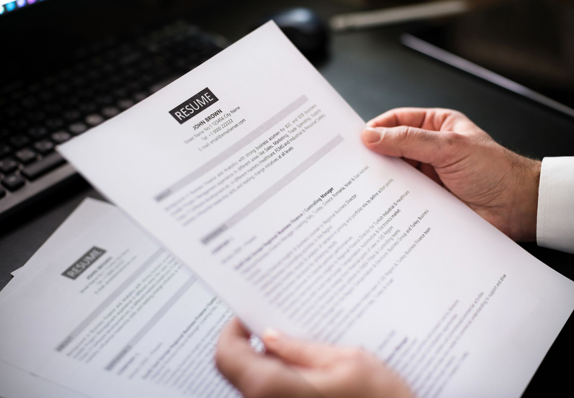 A person is holding a piece of paper with a resume on it.