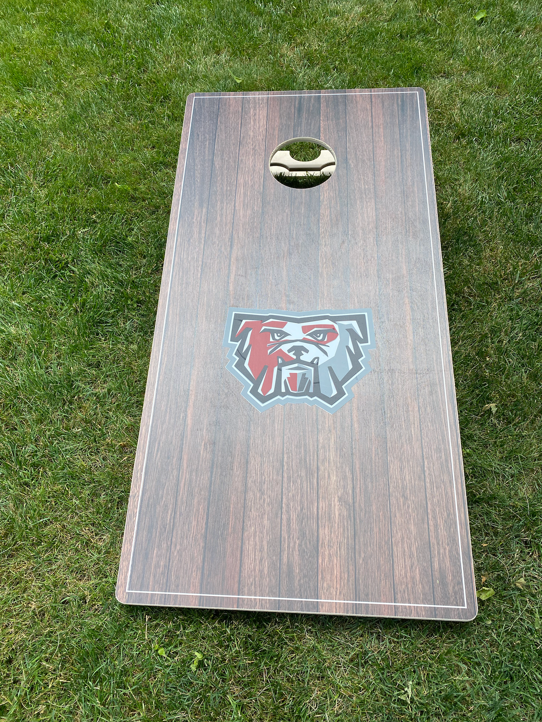 A wooden cornhole board is sitting on top of a lush green field.