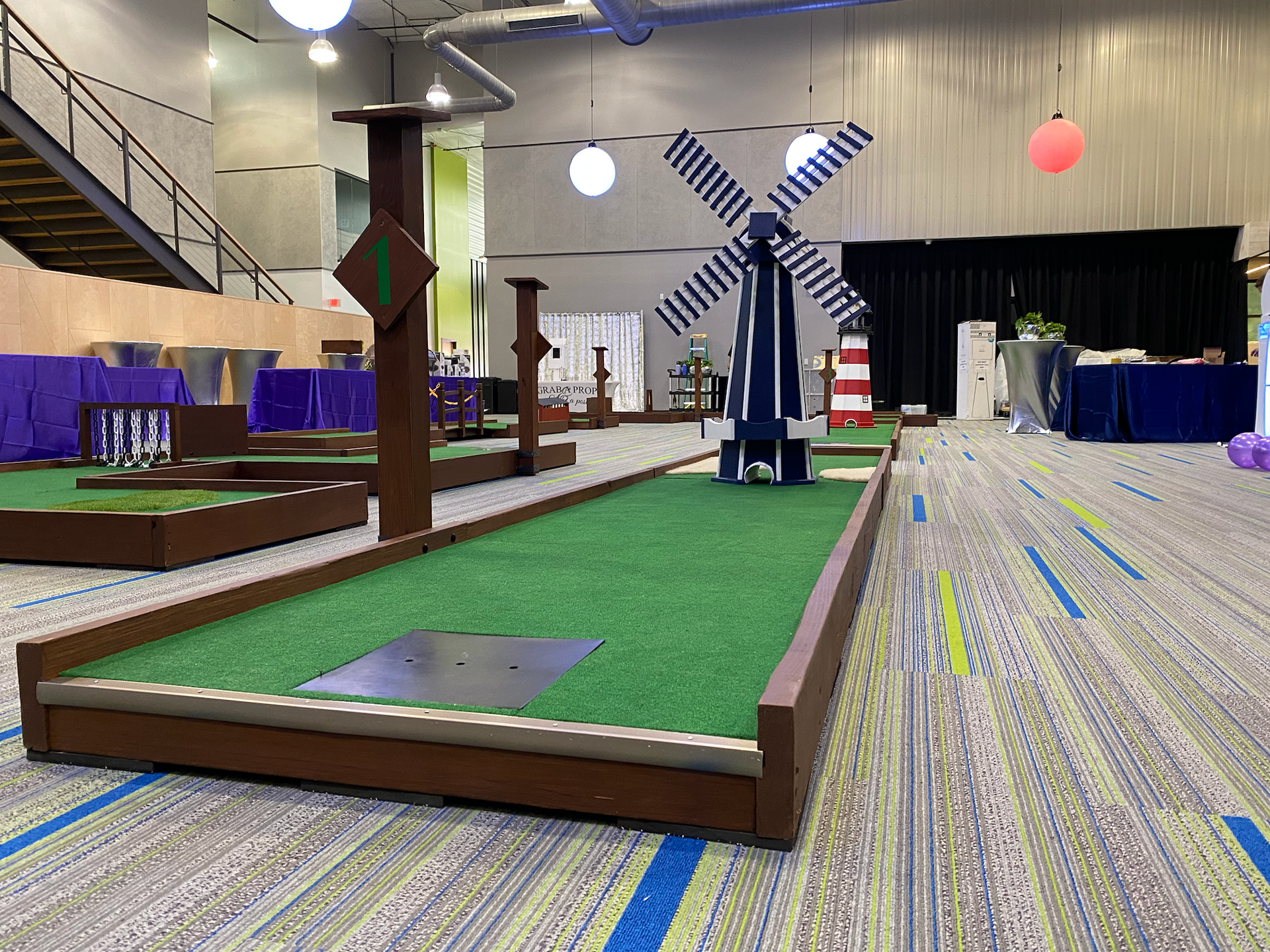 A mini golf course with a windmill in the middle of it in a large room.