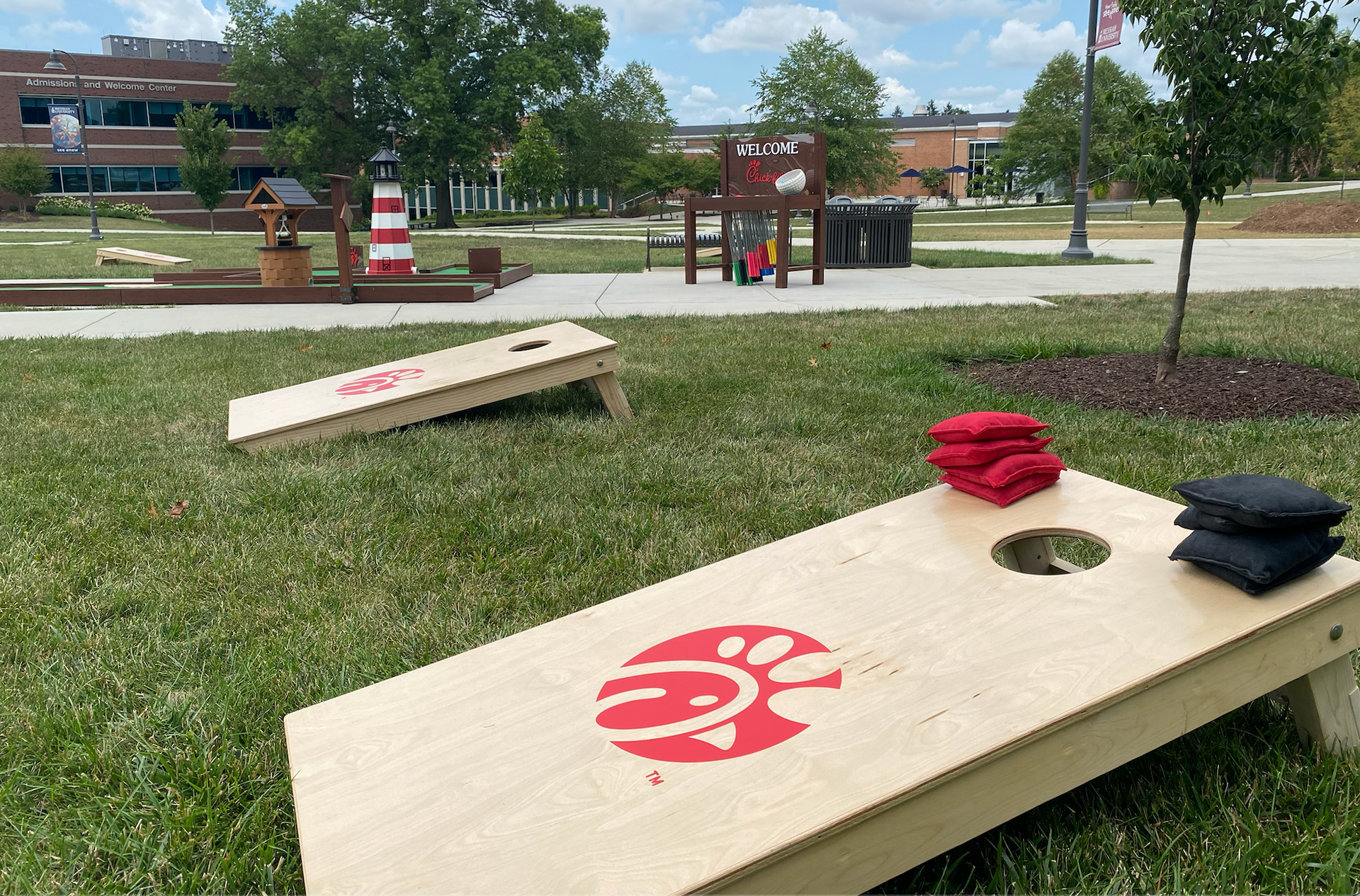 A wooden cornhole board is sitting in the grass in a park.
