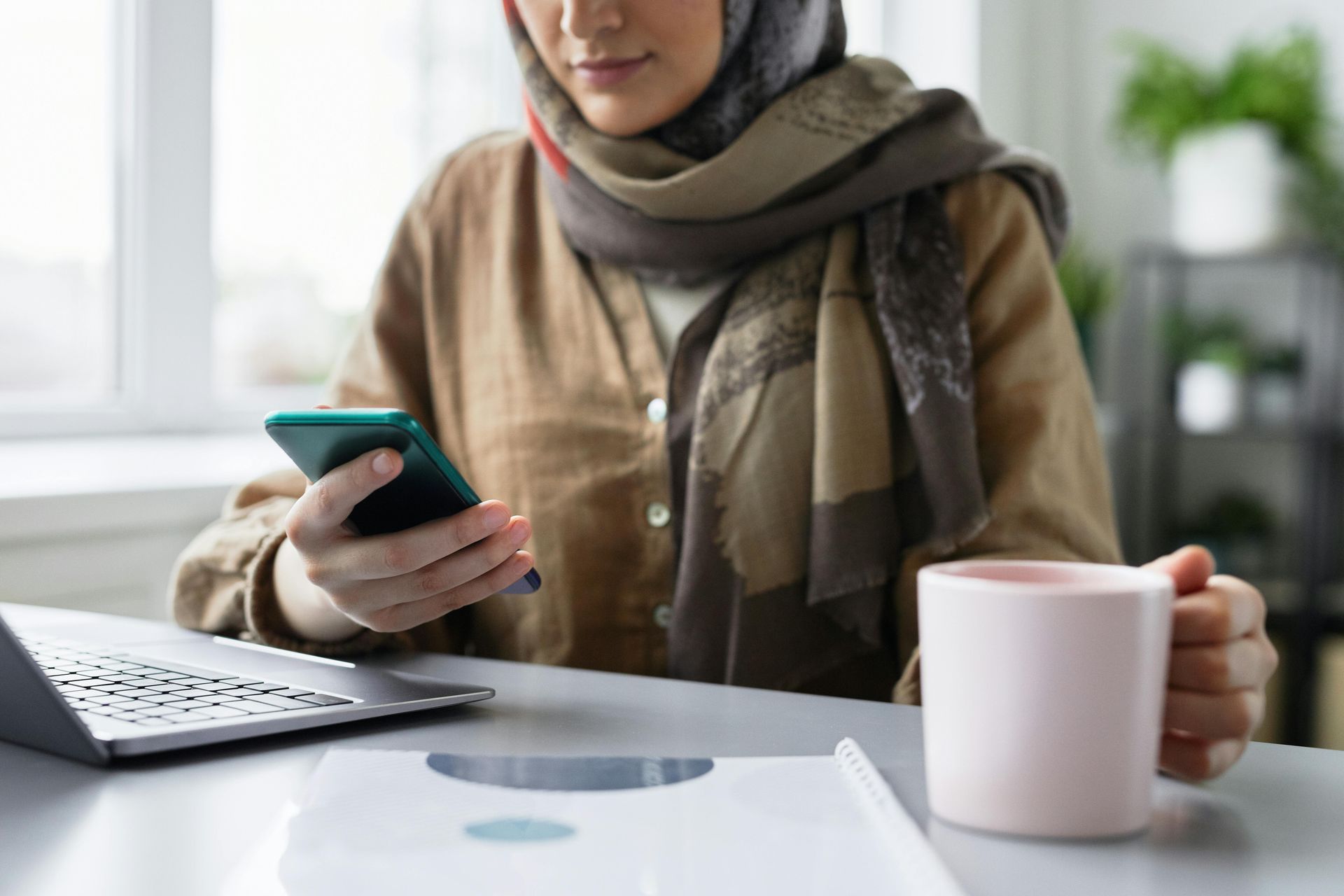woman scrolling their phone with cup in her hand