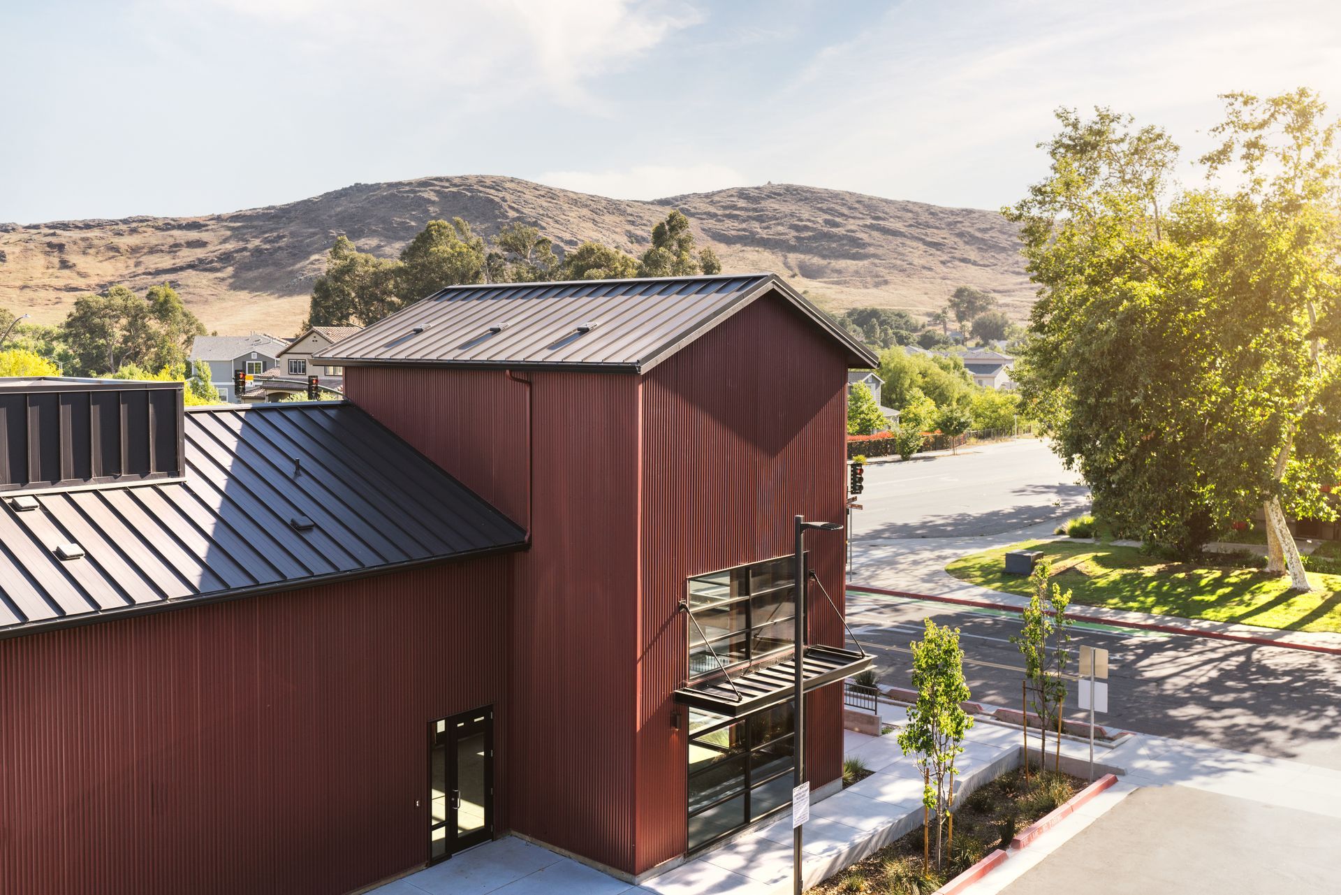 An aerial view of a red building with a black roof and mountains in the background.