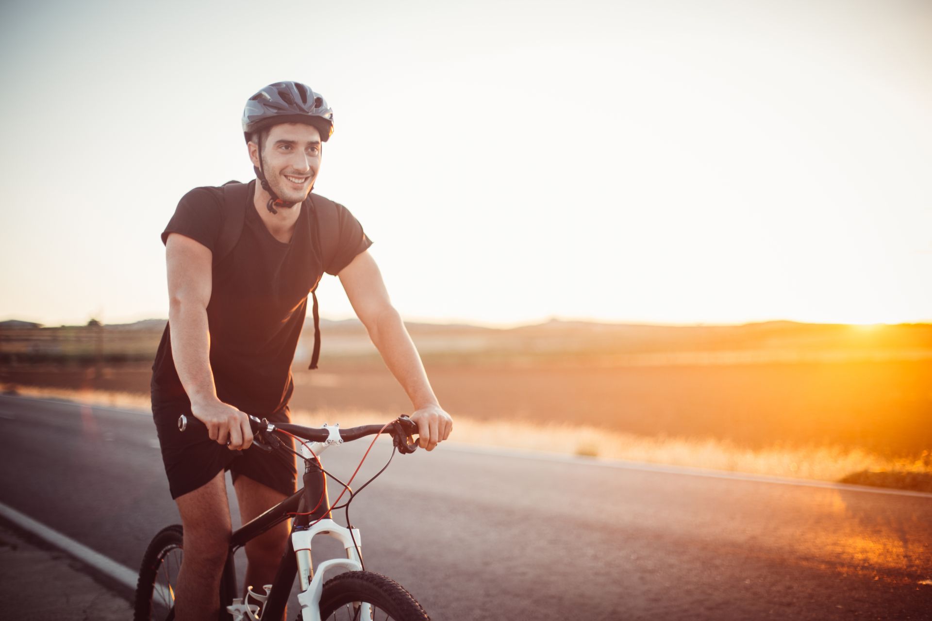 A man is riding a bike down a road at sunset.