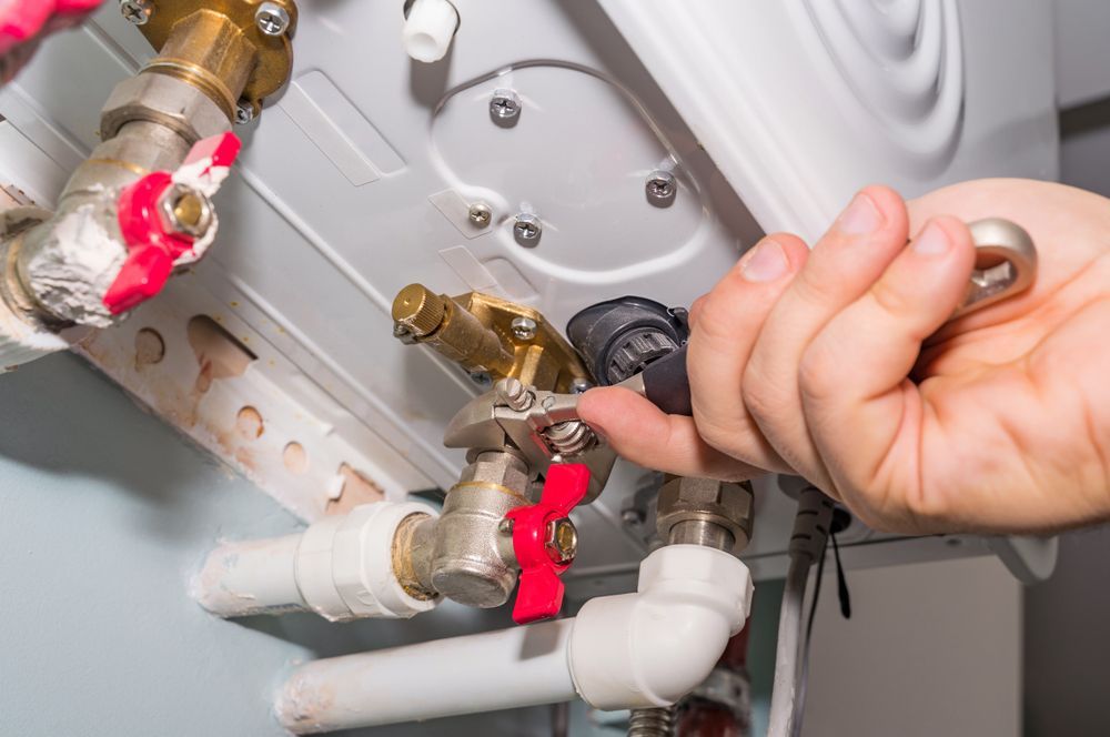 A Person is Fixing a Water Heater With a Wrench — Chad Warrington Plumbing In New Lambton, NSW