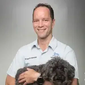 Smiling veterinarian in a white polo holding a fluffy black dog against a gray background
