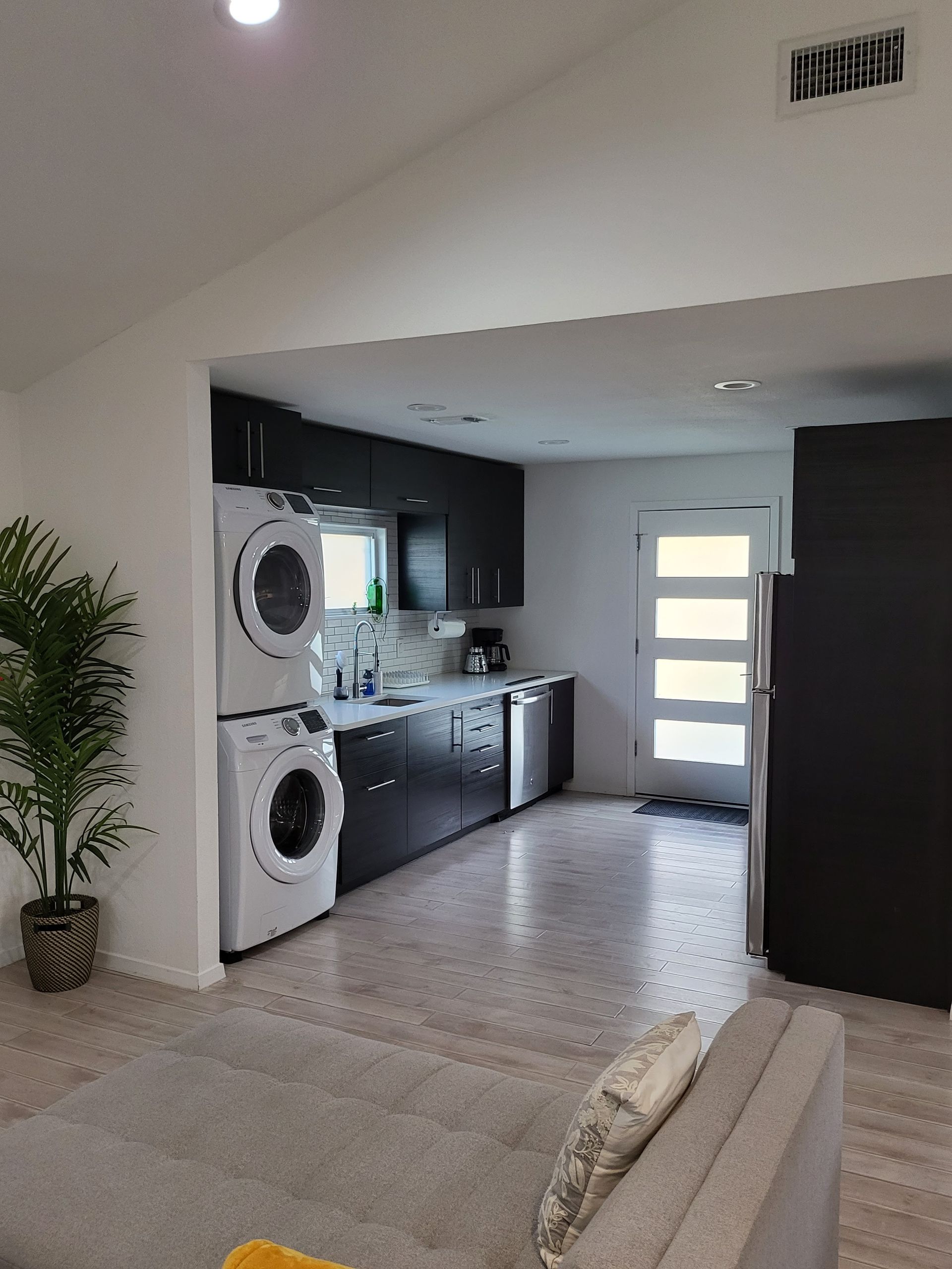 Living room with staircase, adjacent laundry and kitchen area, and a glass-paneled front door