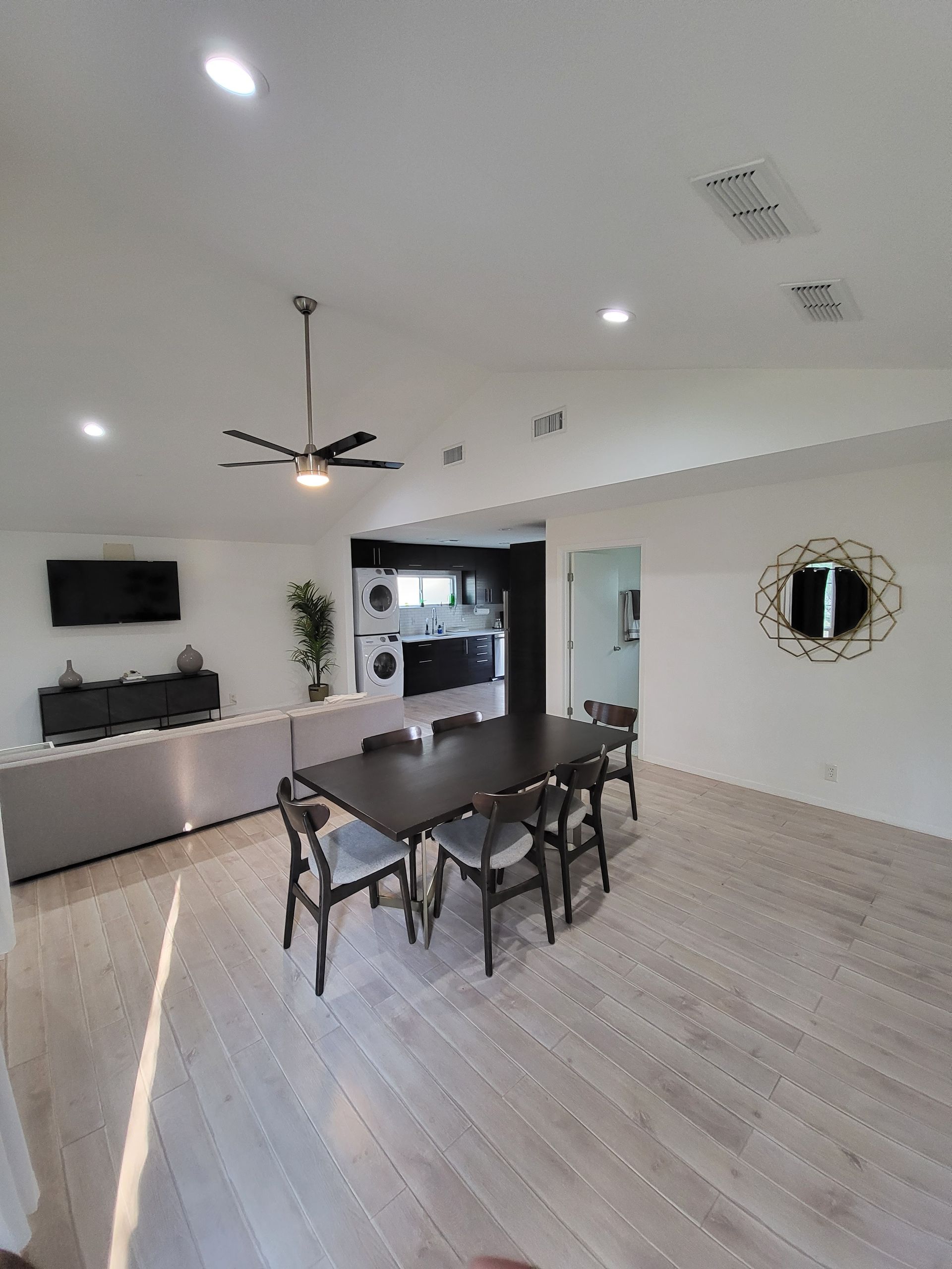 Modern dining room with dark table, chairs, ceiling fan, wall TV, and large mirror on a light wood floor