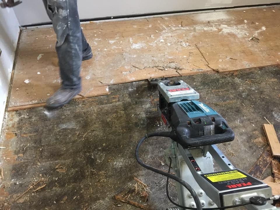 Person walking across a partially stripped floor with a floor sanding machine in the foreground.