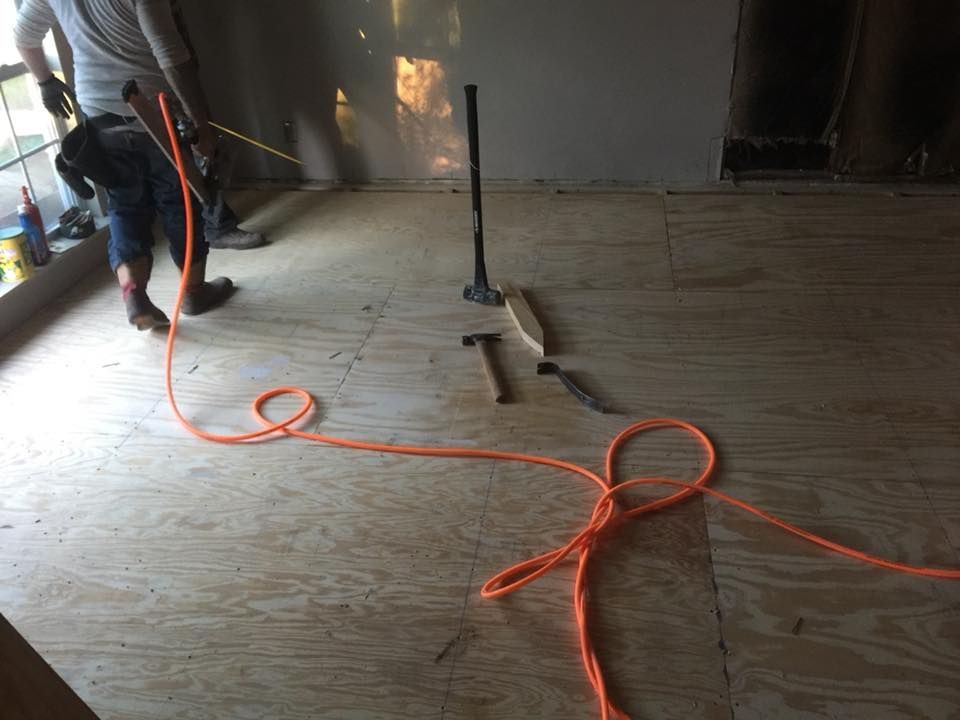 Worker vacuuming wood floor in a room under construction with an orange cord on the floor
