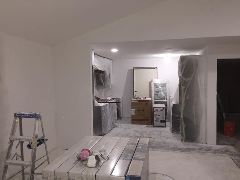 Renovation site with a ladder, covered doorways, and drywall tools in a white room.