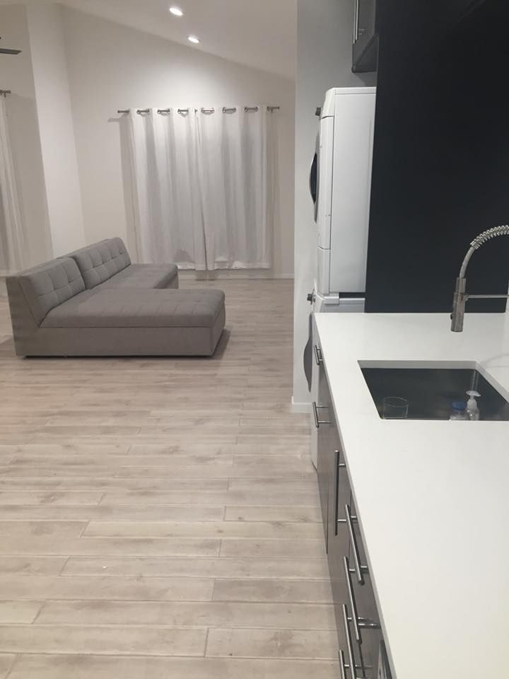 Modern open-plan living room and kitchen with gray sofa, white cabinets, and light wood flooring.