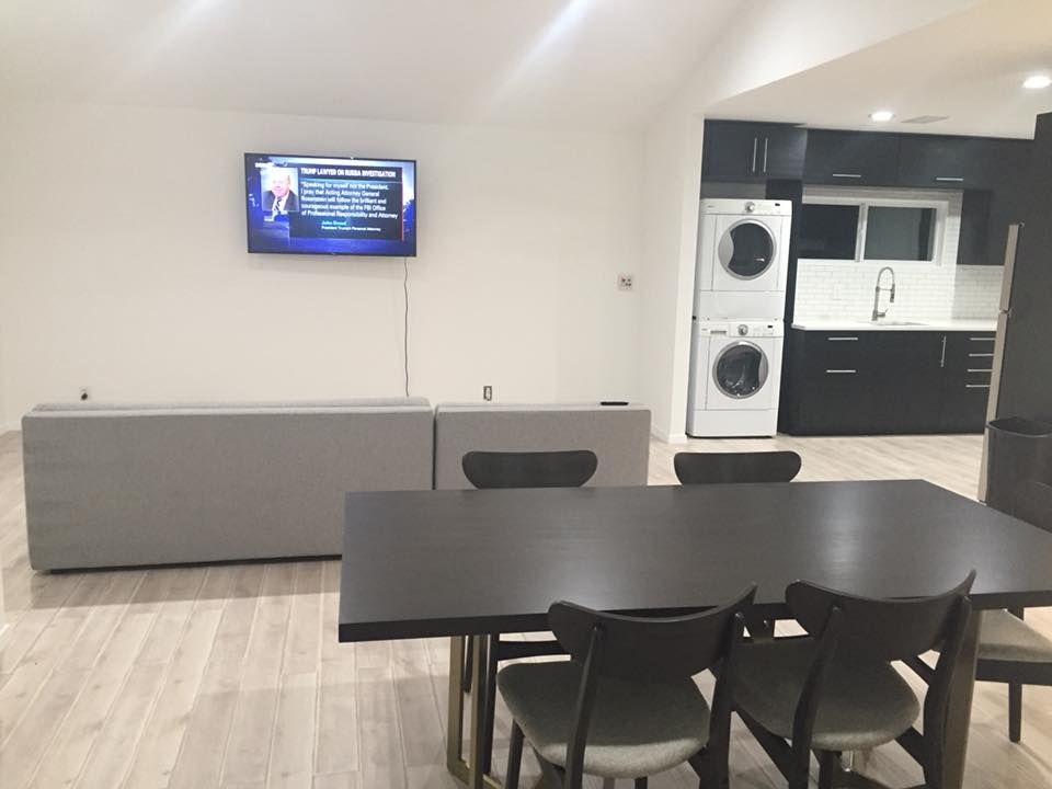 Modern kitchen-dining area with black table, chairs, wall TV, and laundry appliances встроенно to the right
