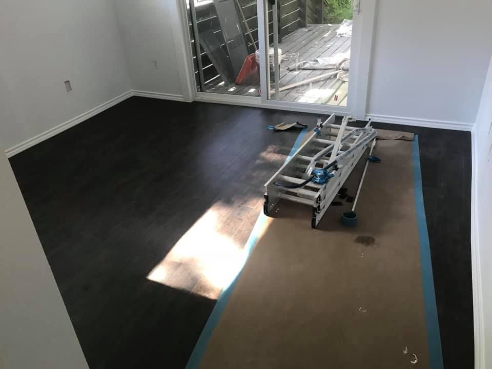 Empty room with black flooring being installed, tools and materials on a tarp by a sliding glass door.