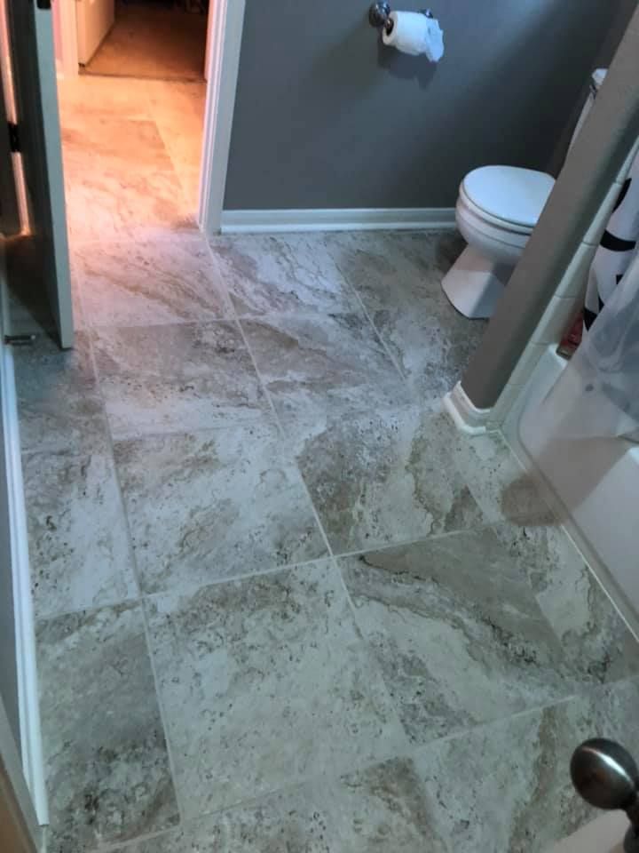 Bathroom with gray tile floor, white toilet, and a doorway leading to a lit room.