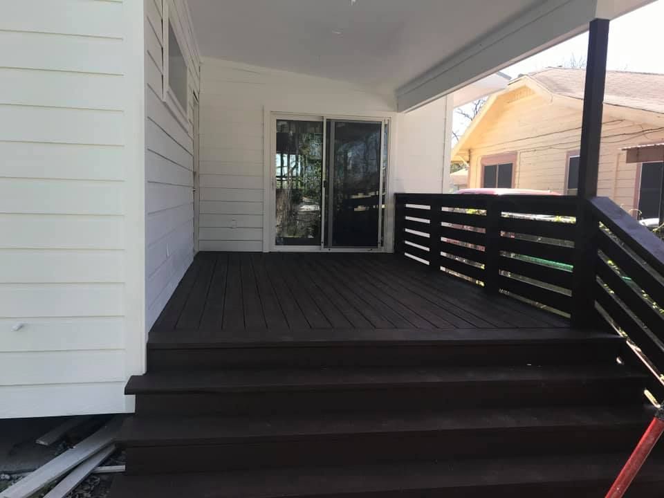 Covered front porch with dark wood deck, steps, and railing leading to sliding glass doors