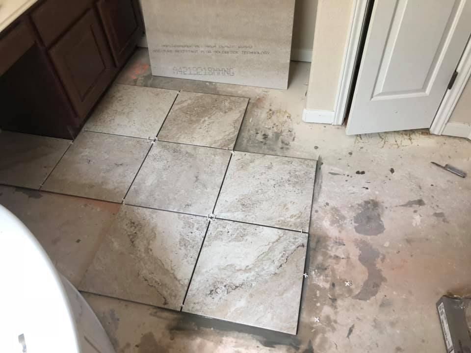 Damaged bathroom floor tiles with stains and debris near an open door