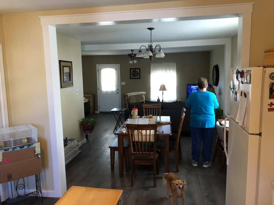 Dining room and kitchen view with a person in a blue shirt standing by the counter and a small dog on the floor.