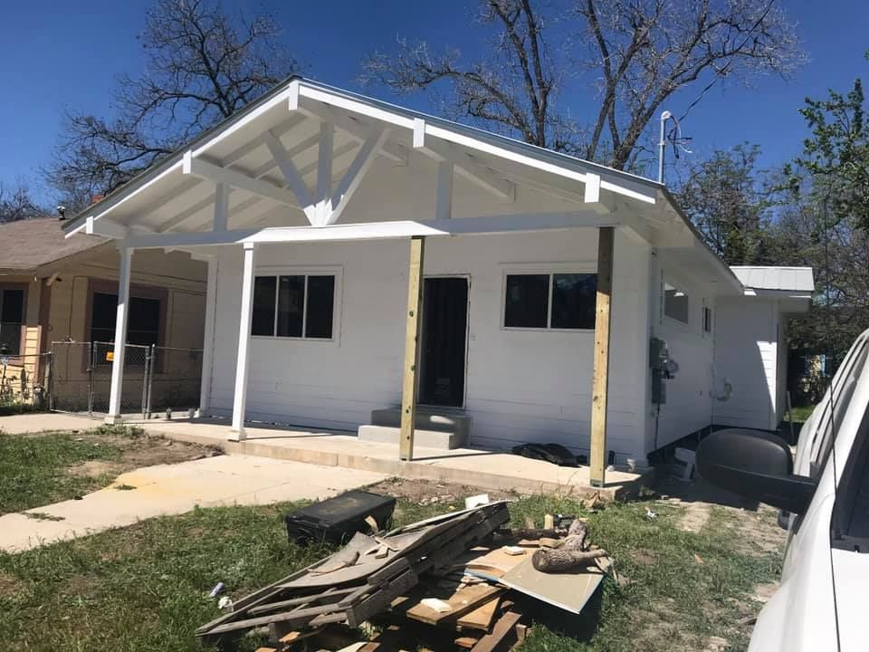 Small white house with a front porch and construction debris in the yard under a clear blue sky