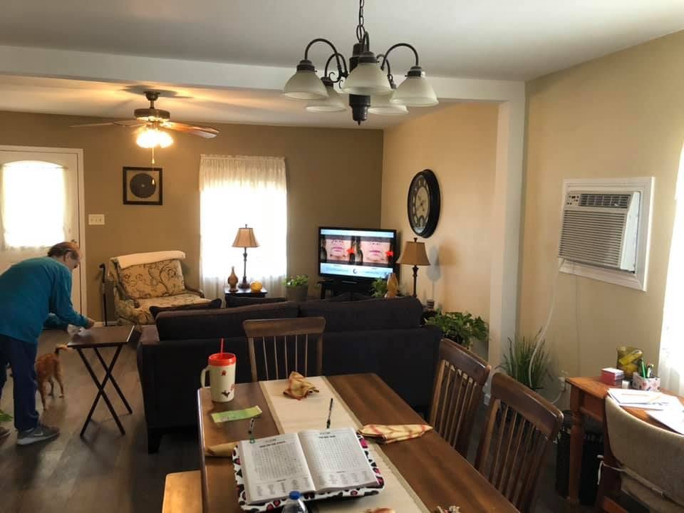 Living room with TV, dining table, and a person bending over near a window