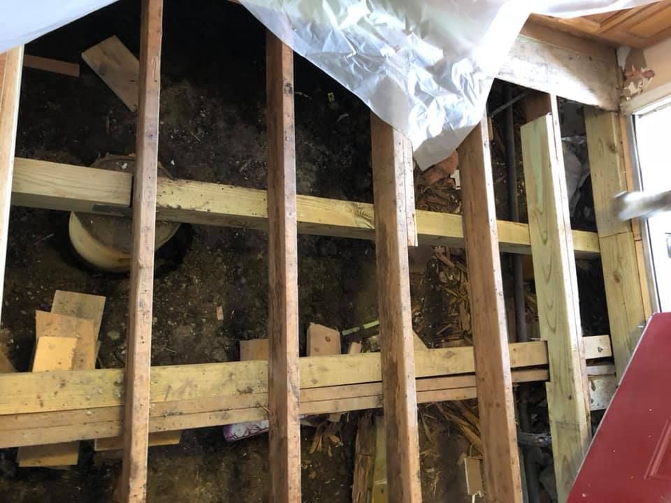 Exposed wooden wall framing with insulation and plastic sheeting in a construction area