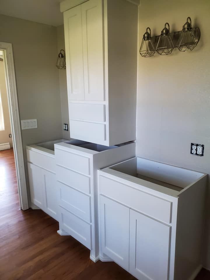 Empty laundry room with white cabinets and two gray laundry sink basins on hardwood flooring