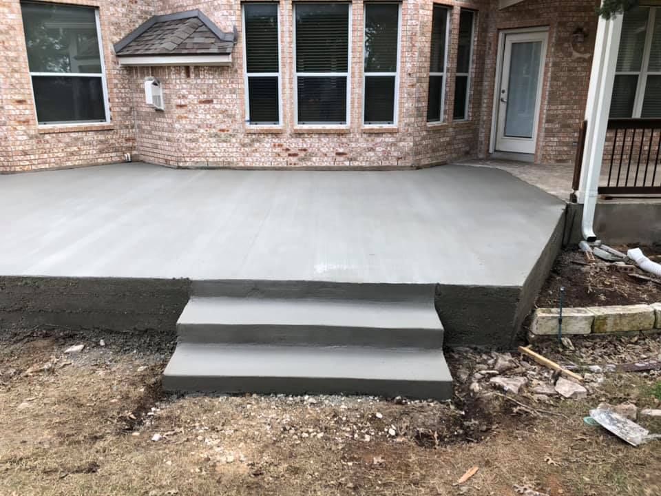 Concrete backyard patio with three steps leading up to a brick house