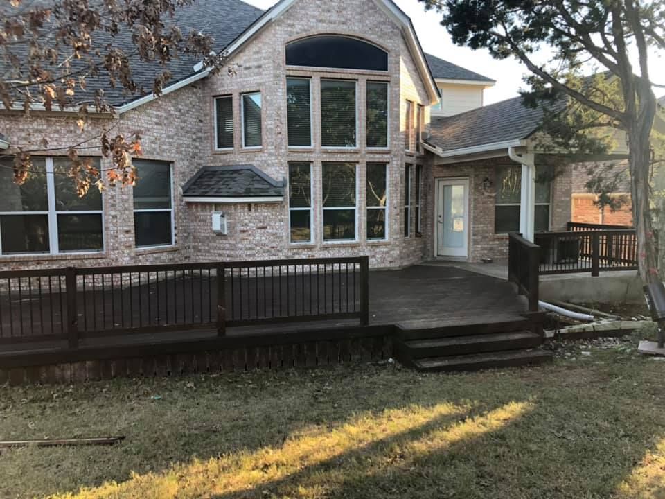 Stone house with large windows and a raised wooden deck in a backyard.