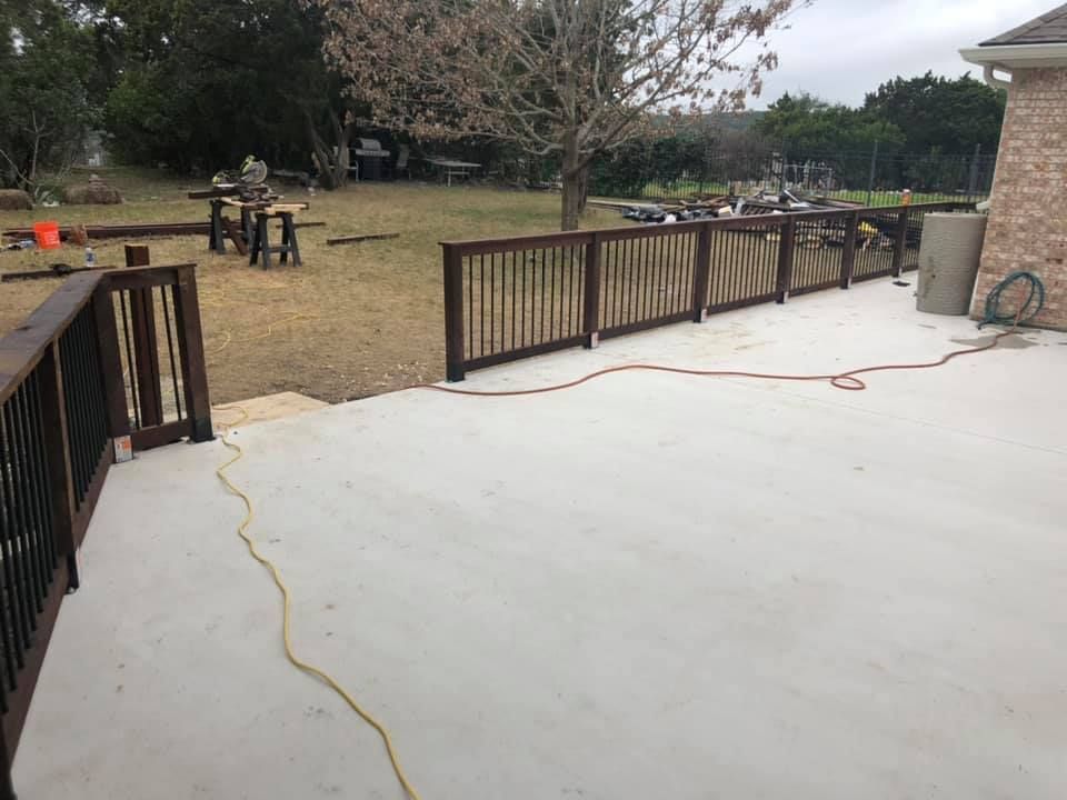 Back deck with wooden railings and a large open yard beyond, concrete patio in foreground.