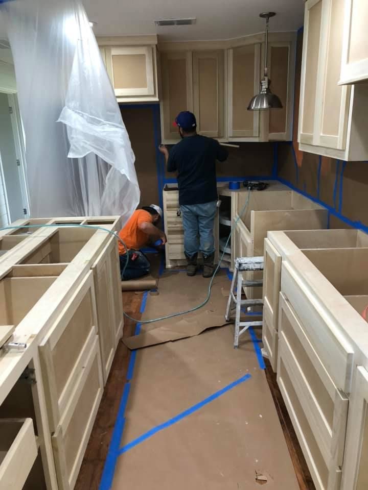 Two workers installing cabinets in a kitchen, with blue painter’s tape on floors and counters.