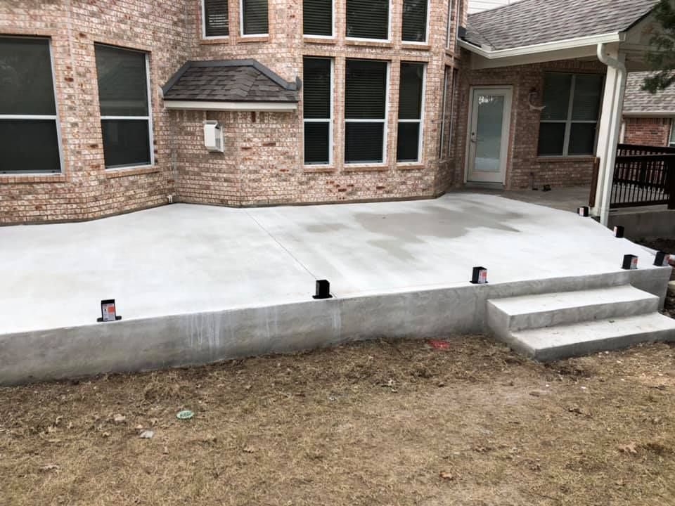 Raised concrete patio with steps beside a brick house, viewed from the yard.