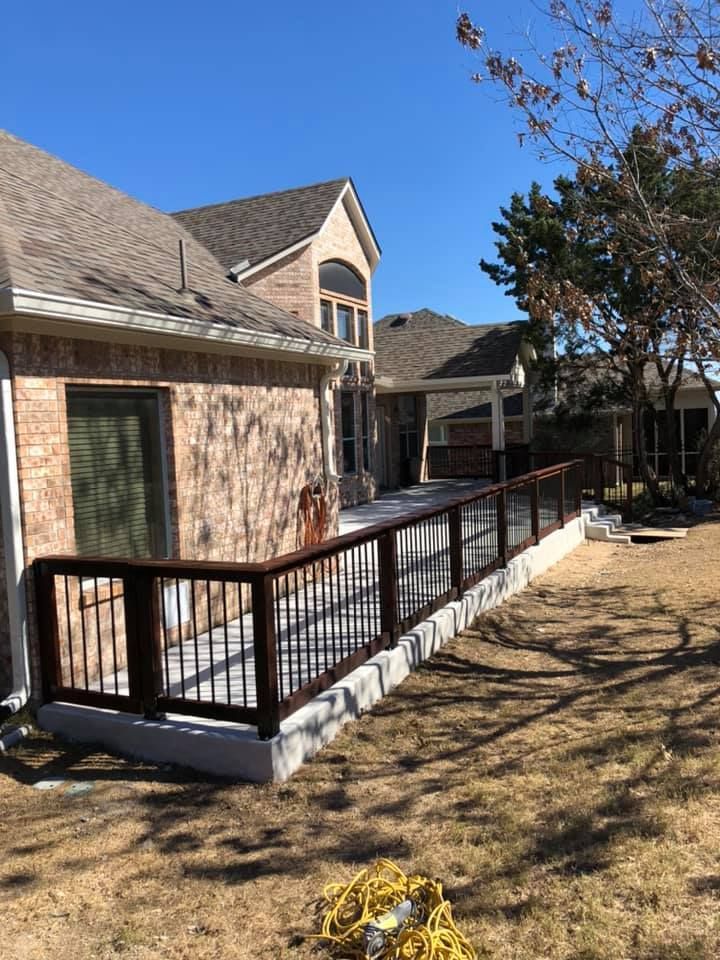 Backyard stone patio with a wooden ramp and black railings beside a brick house