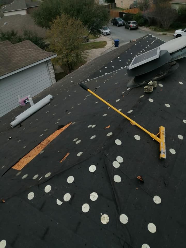 Roof with dark shingles and scattered white patches, with a yellow pipe and nearby vent under a cloudy sky