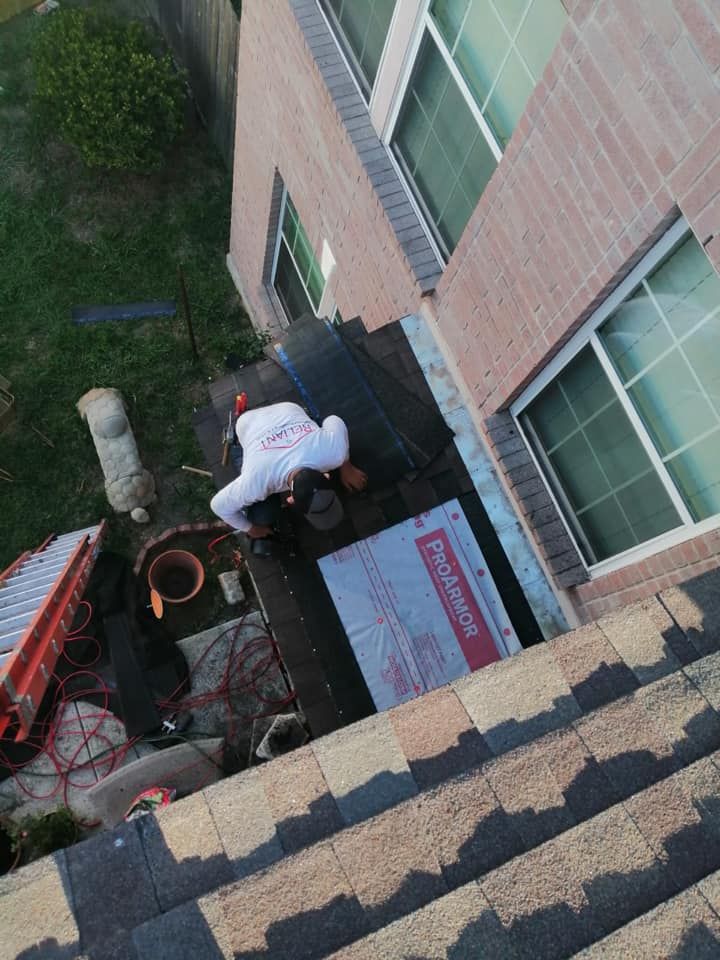 Worker on a rooftop next to a building, handling equipment near windows and shingles.