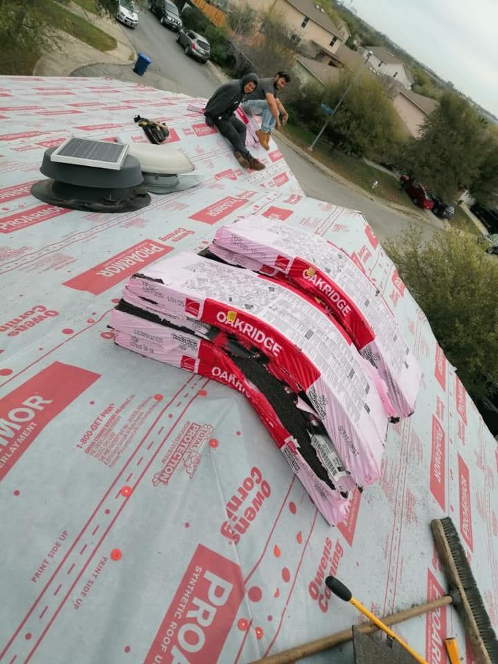 Workers installing pink-and-white roofing shingles on a sloped roof.