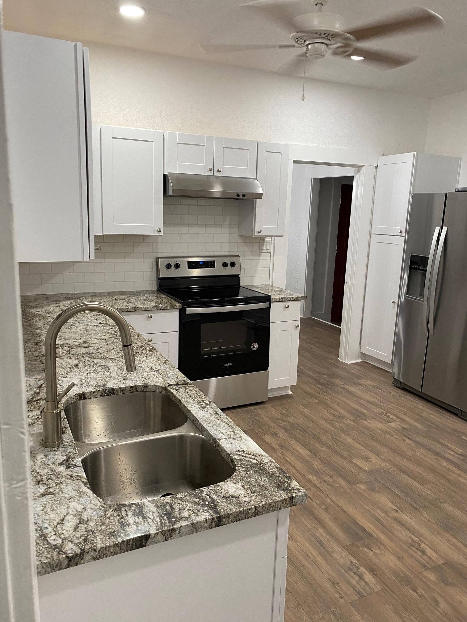 Bright kitchen with white cabinets, granite counters, stainless sink, stove, and refrigerator.