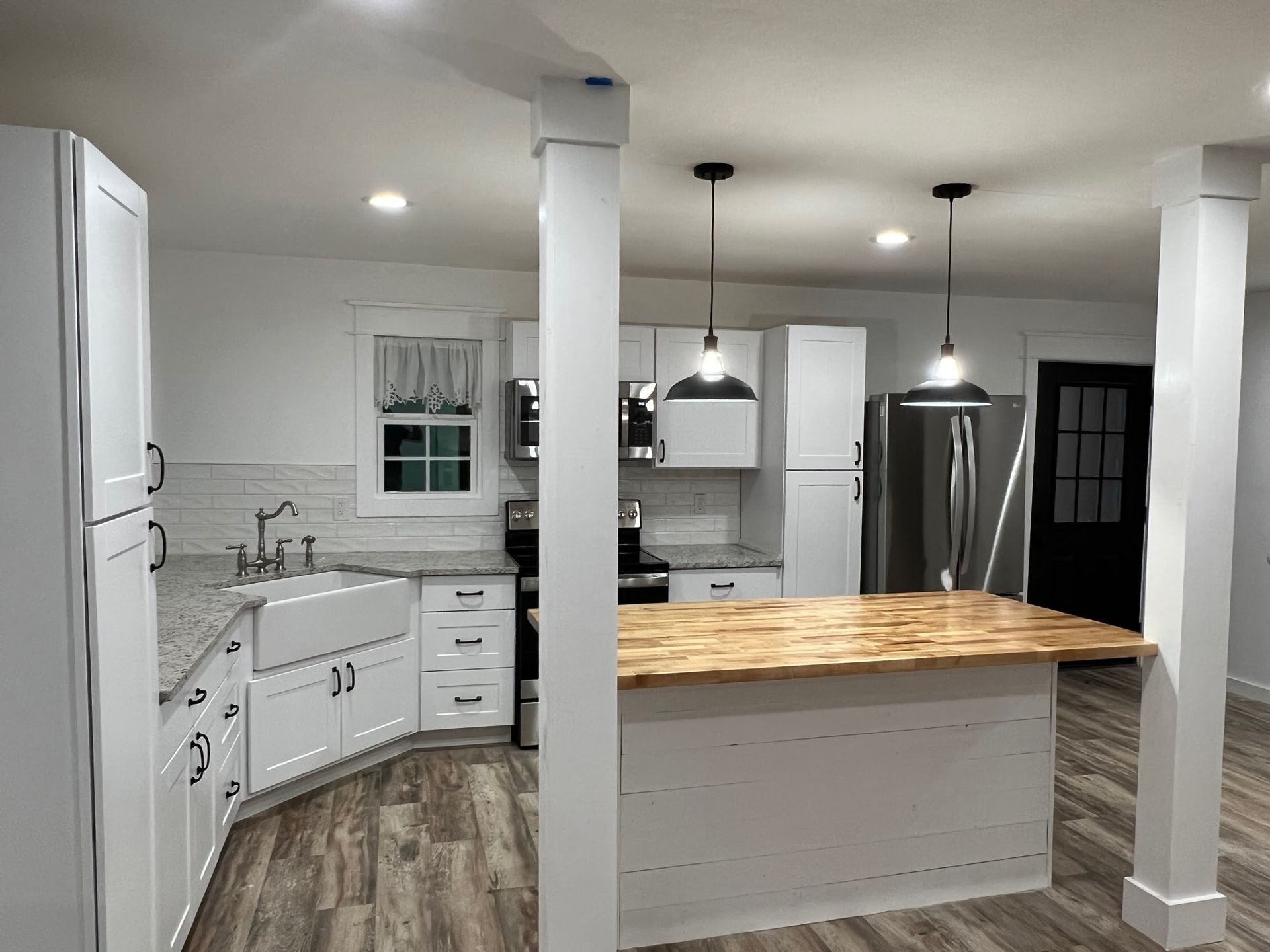 Bright white kitchen with an island, stainless steel fridge, and pendant lights above hardwood floors.