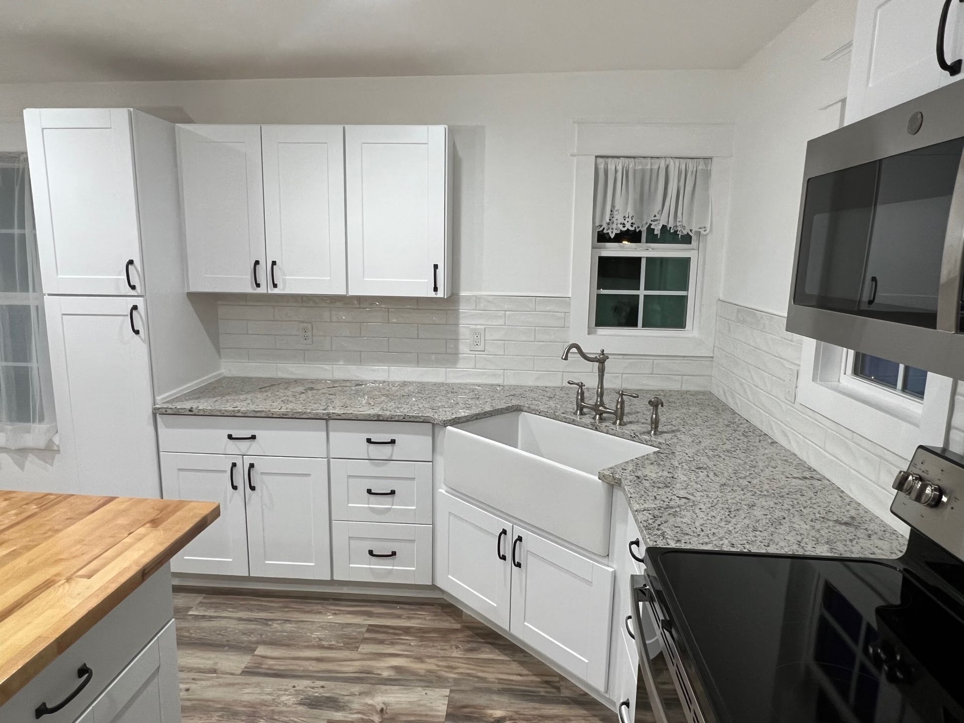 Bright modern kitchen with white cabinets, gray tile backsplash, granite counters, and wood-look floor