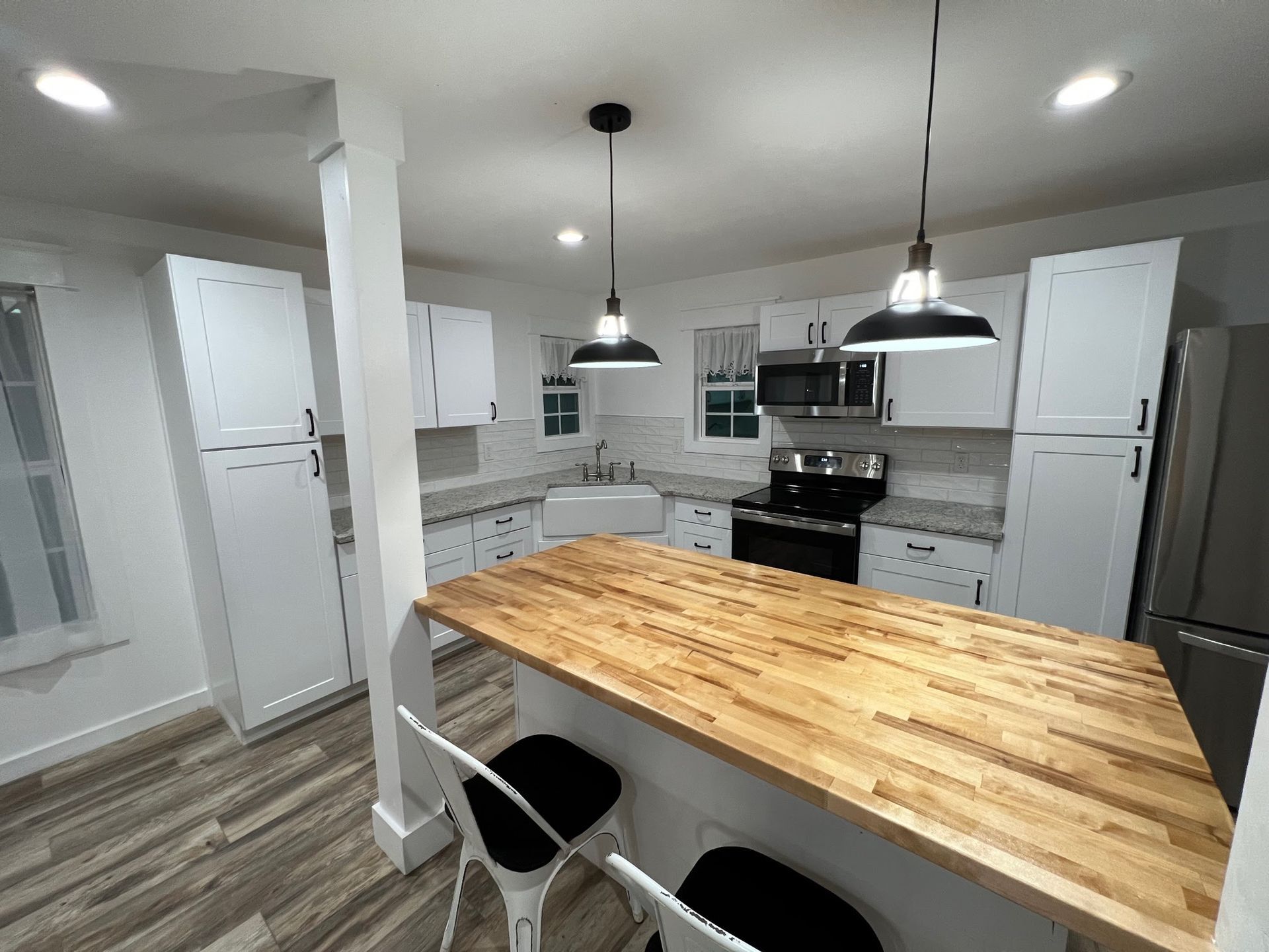 Bright modern kitchen with white cabinets, black appliances, and a large wooden island with pendant lights.
