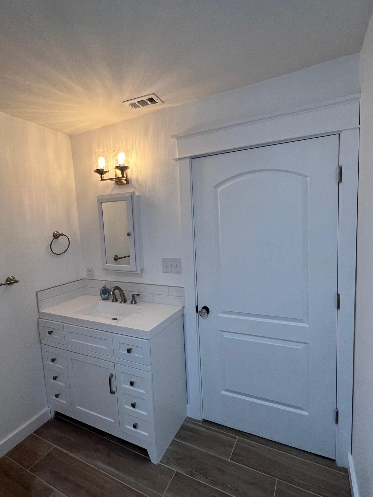 A bathroom with a sink , mirror and door.
