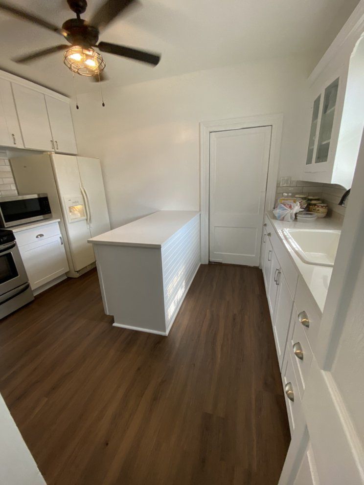 Bright white galley kitchen with wood floors, island, and stainless appliances