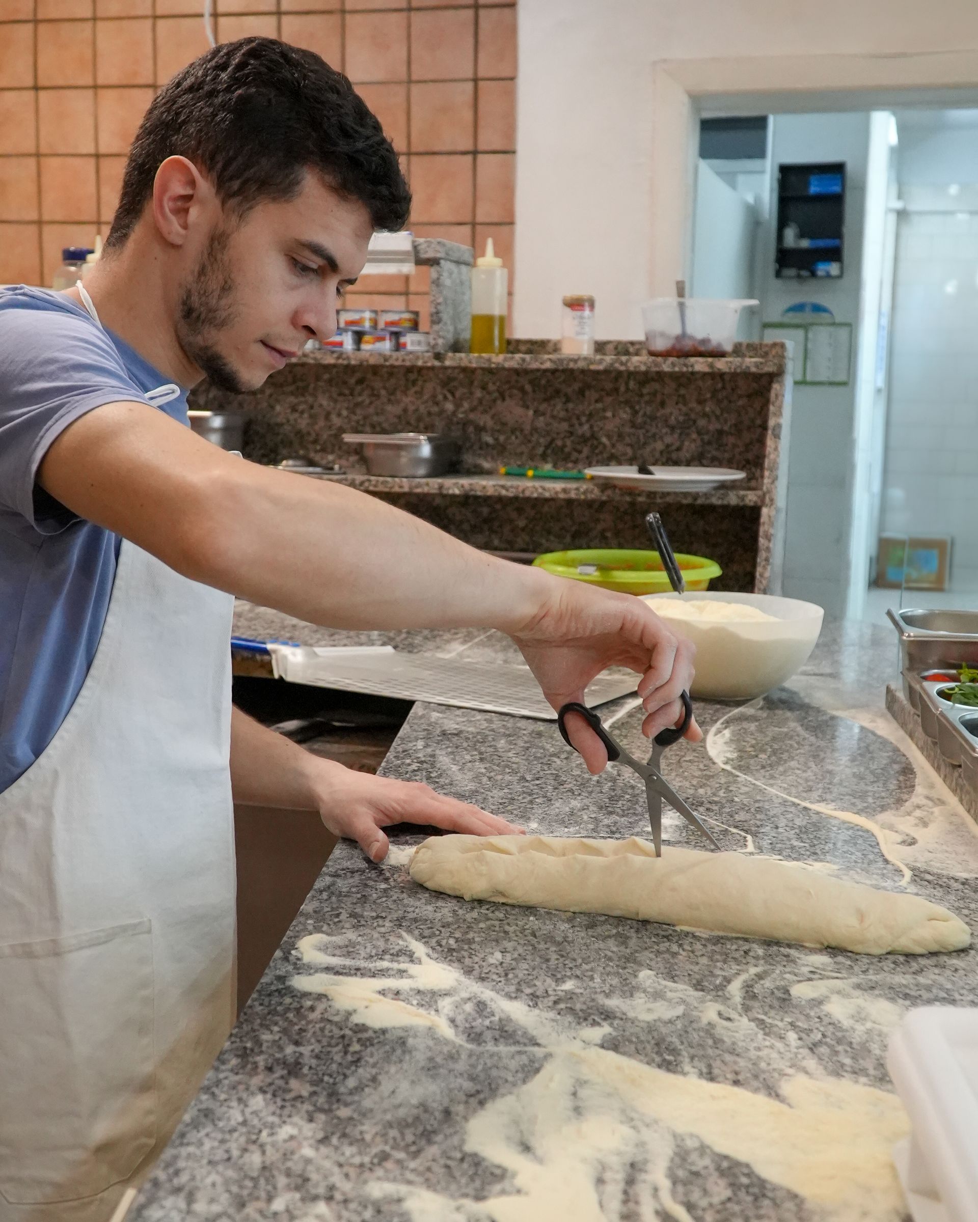 Una persona modella l'impasto su un piano di lavoro infarinato in cucina, usando una spatola vicino a una pagnotta.