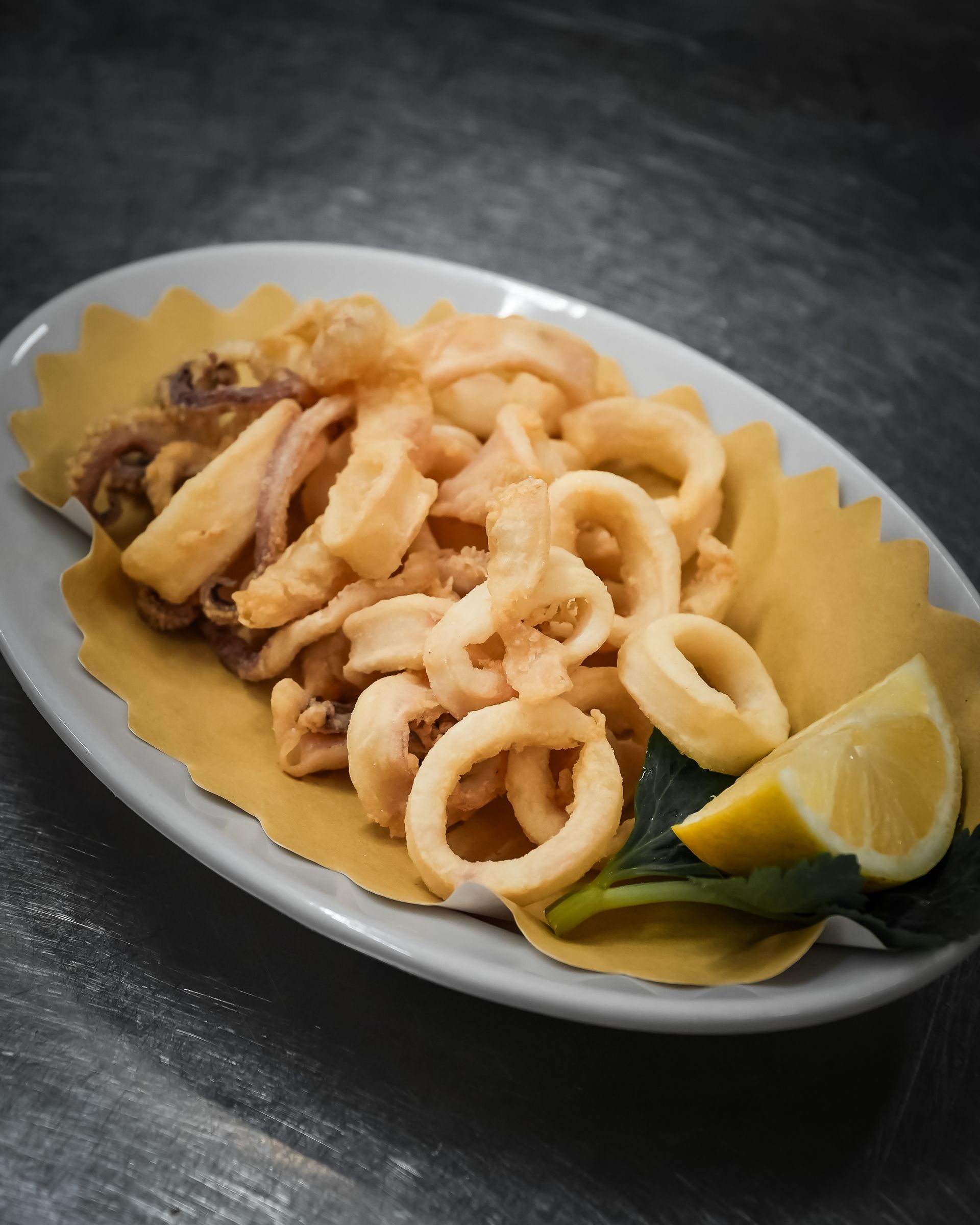 Fried calamari on a white plate with lemon wedges and dipping sauce.