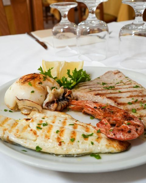 Carne grigliata e frittata ripiena di formaggio su un piatto bianco in un ambiente da ristorante.