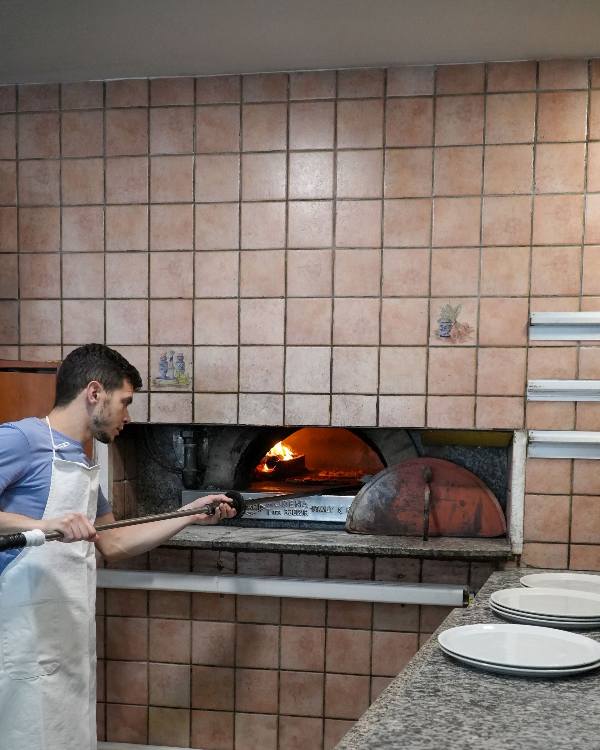Un uomo inforna una pizza in un forno a legna in una pizzeria piastrellata.