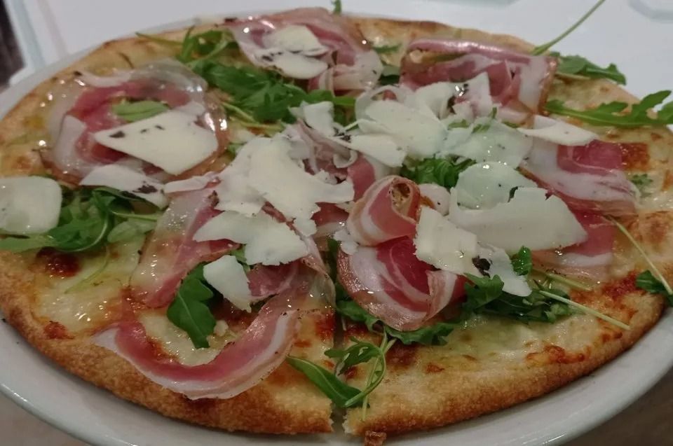 Pizza condita con rucola, prosciutto e formaggio grattugiato su un piatto bianco