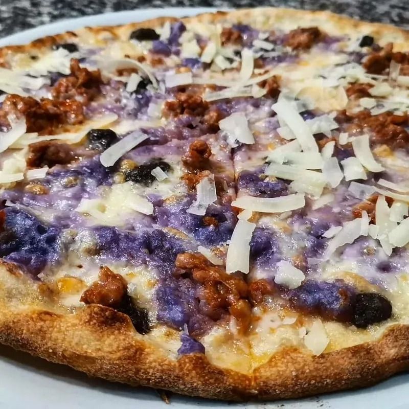 Primo piano di una pizza al formaggio con cipolla rossa, olive e salsiccia sbriciolata su una crosta dorata.