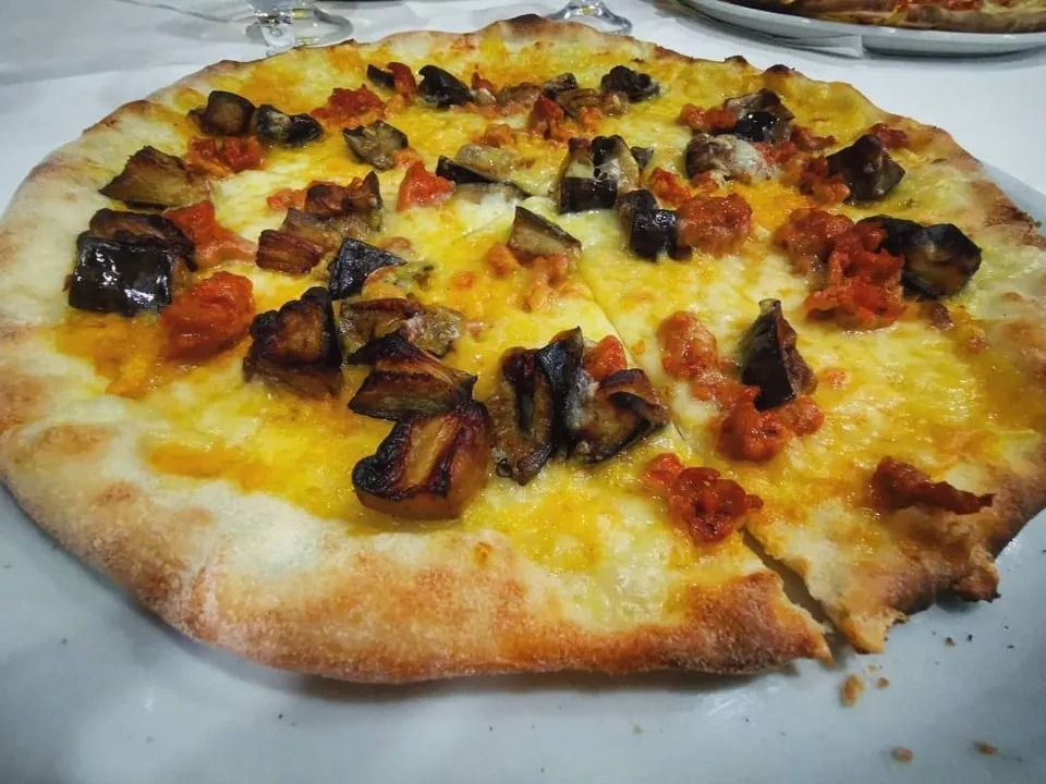 Pizza condita con formaggio fuso e funghi arrostiti su un piatto bianco.