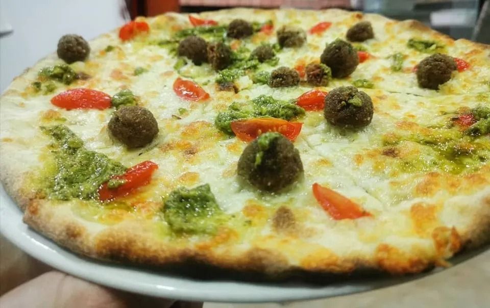 Pizza bianca condita con pesto verde, pomodorini e polpette su un piatto