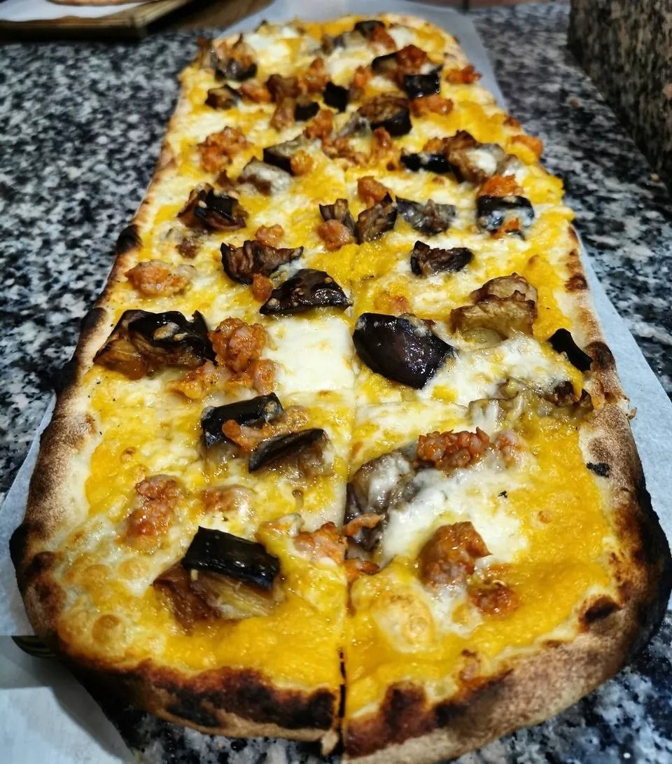 Una pizza rettangolare con formaggio fuso e funghi, adagiata su un piano di lavoro in granito.