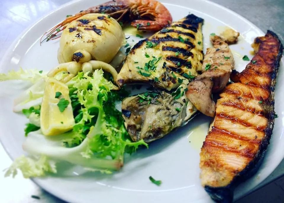 Grilled seafood platter with shrimp, fish, broccoli, mash, and charred vegetables on a white plate